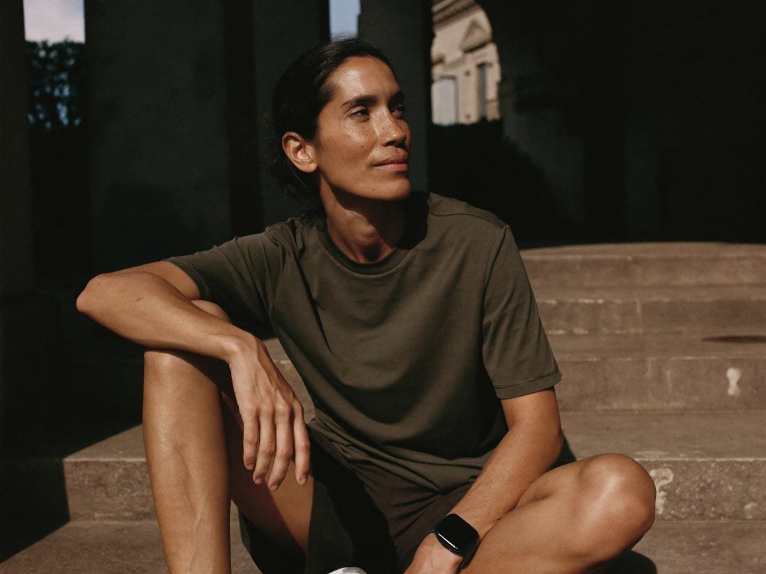 A runner sitting on stone steps after a run, looking out across a sunlit courtyard.